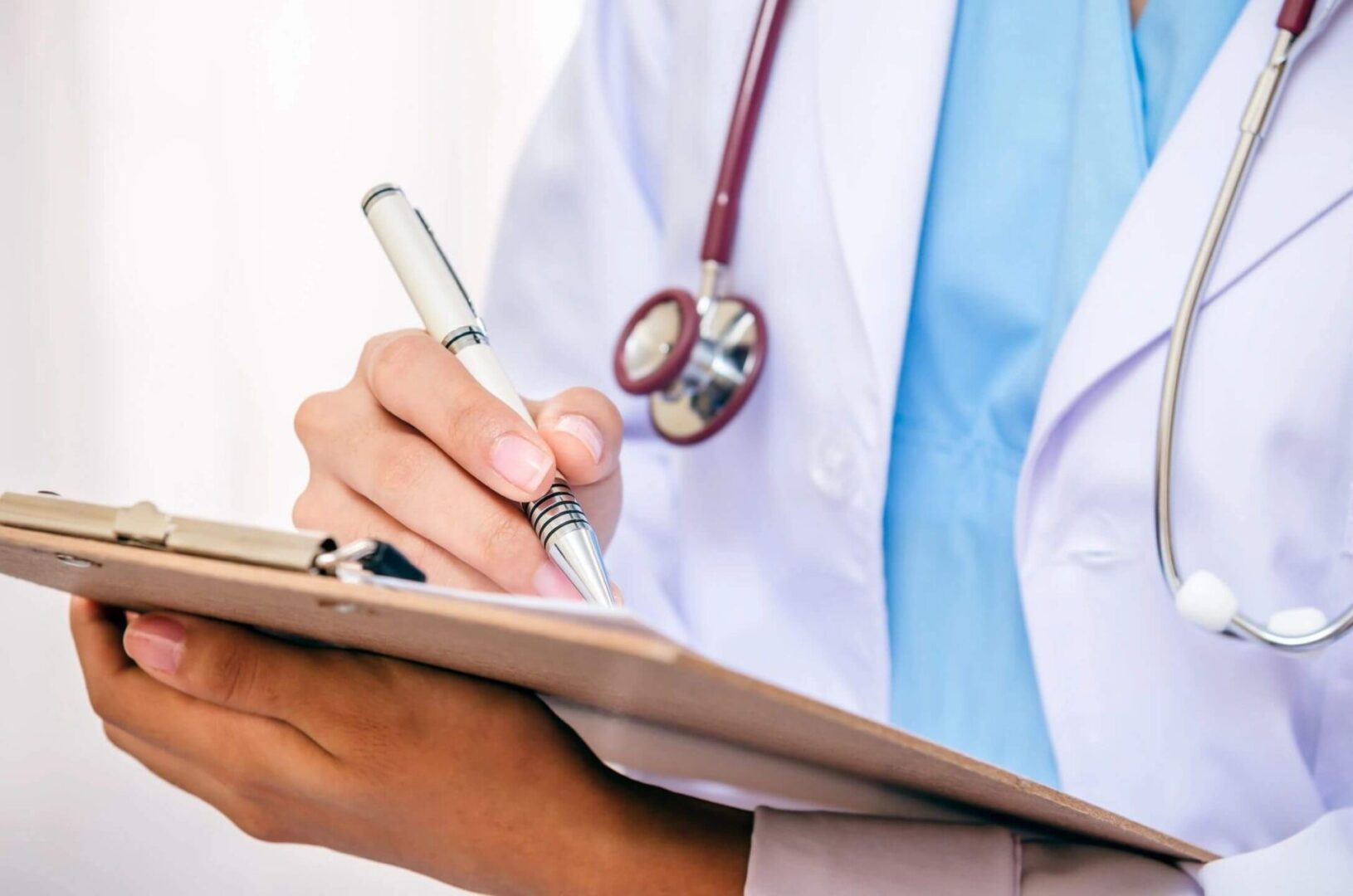 A doctor writing on a clipboard with stethoscope around neck.